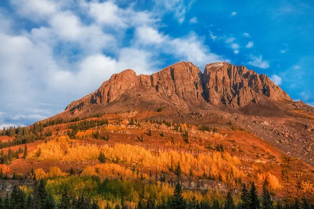 Golden aspens beneath a sunlit red mountain