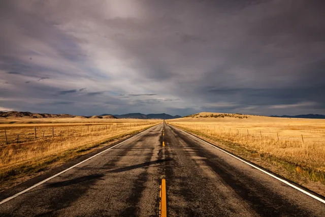 Golden prairie road beneath storm clouds